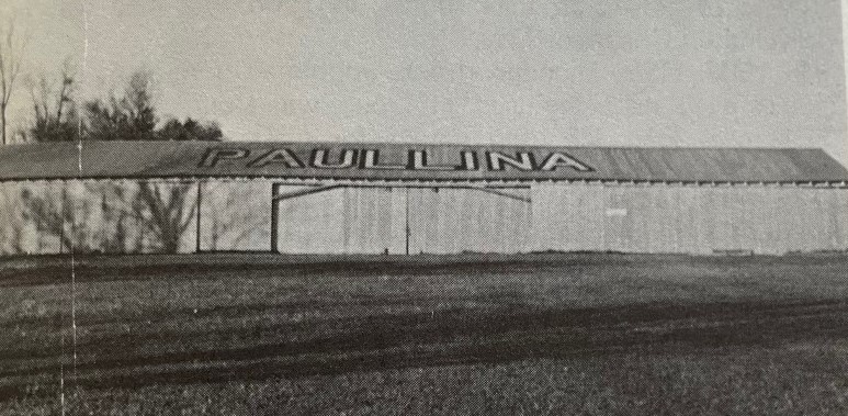 Black and white photo of a large, low building with "Paulina" in bold letters on the roof.