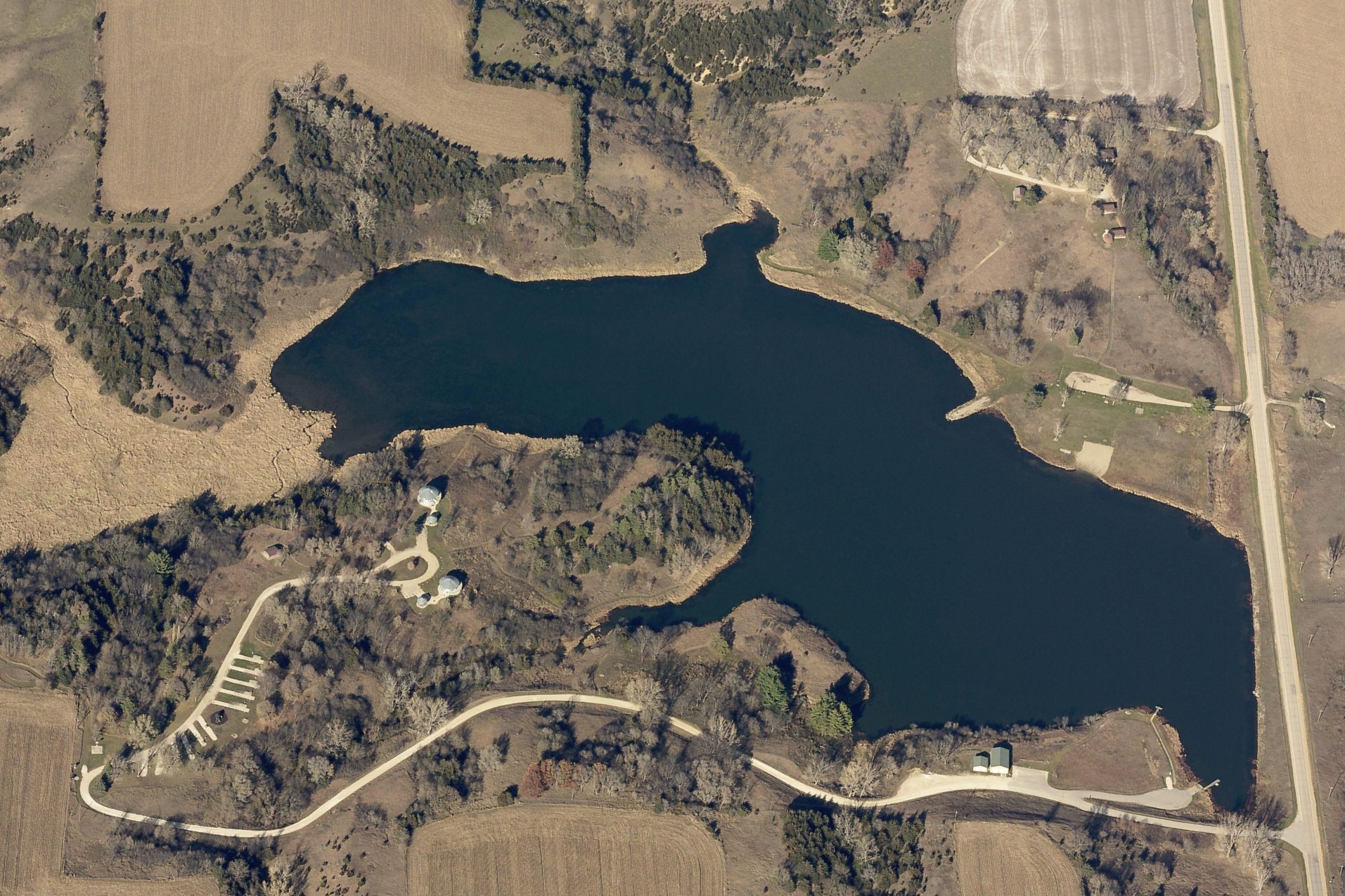 Aerial view of a vast, blue lake surrounded by fields and sparse trees.