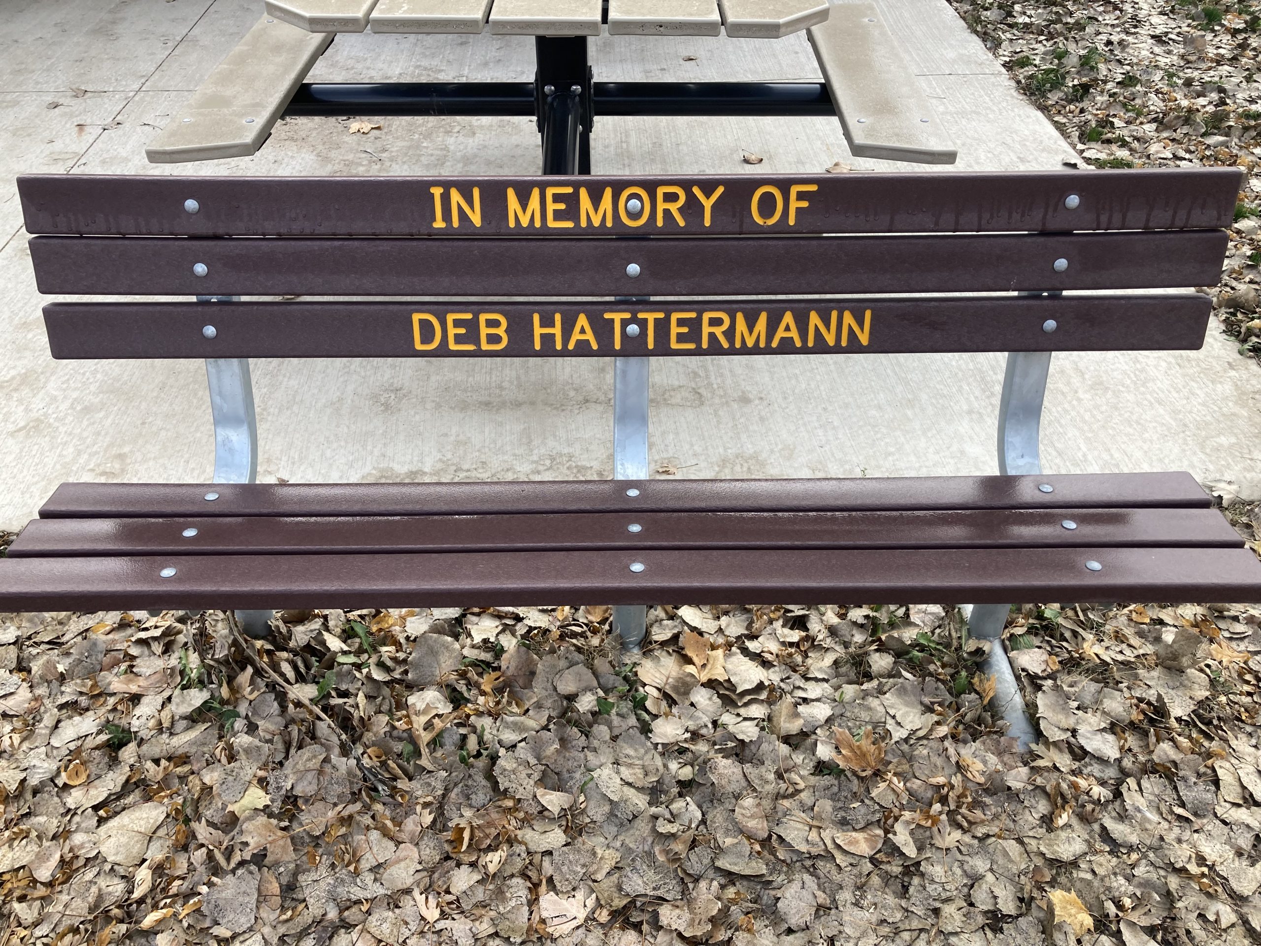 Brown bench with yellow letters that can be purchased for a memorial at a park.