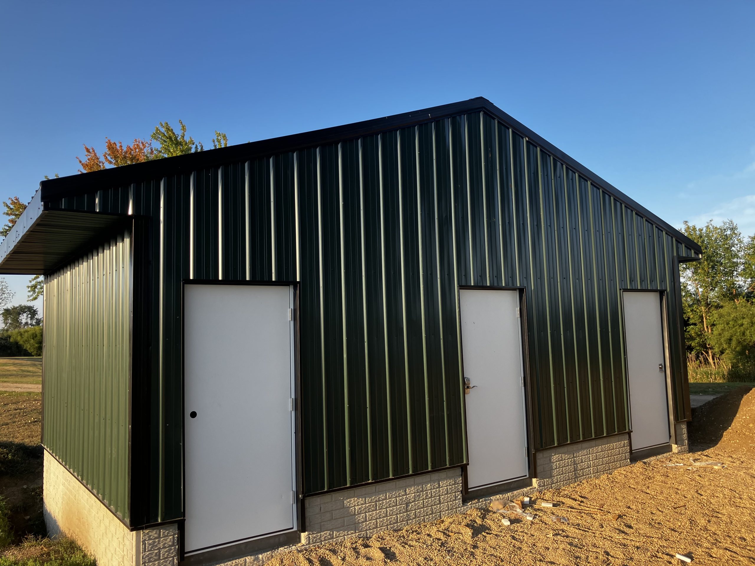A dark green metal shed with three white doors, set against a clear blue sky.