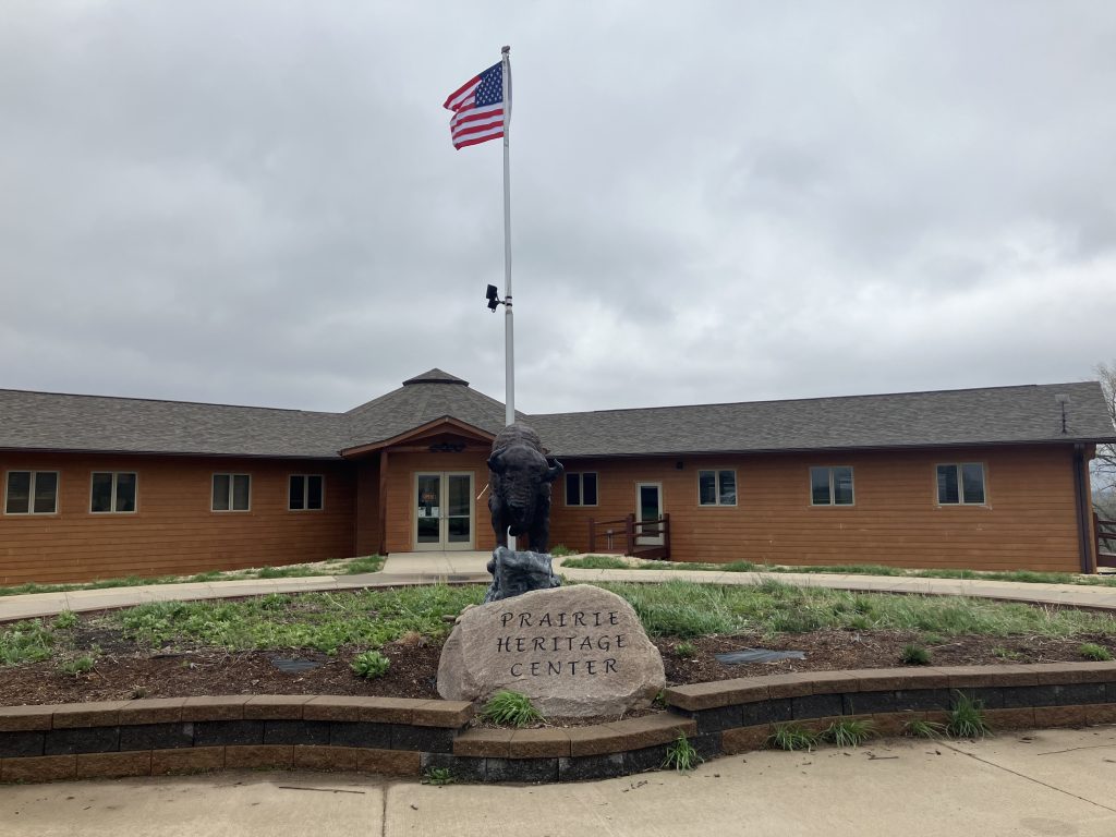 Wooden building with a gabled roof under a cloudy sky. An American flag flies on a pole.