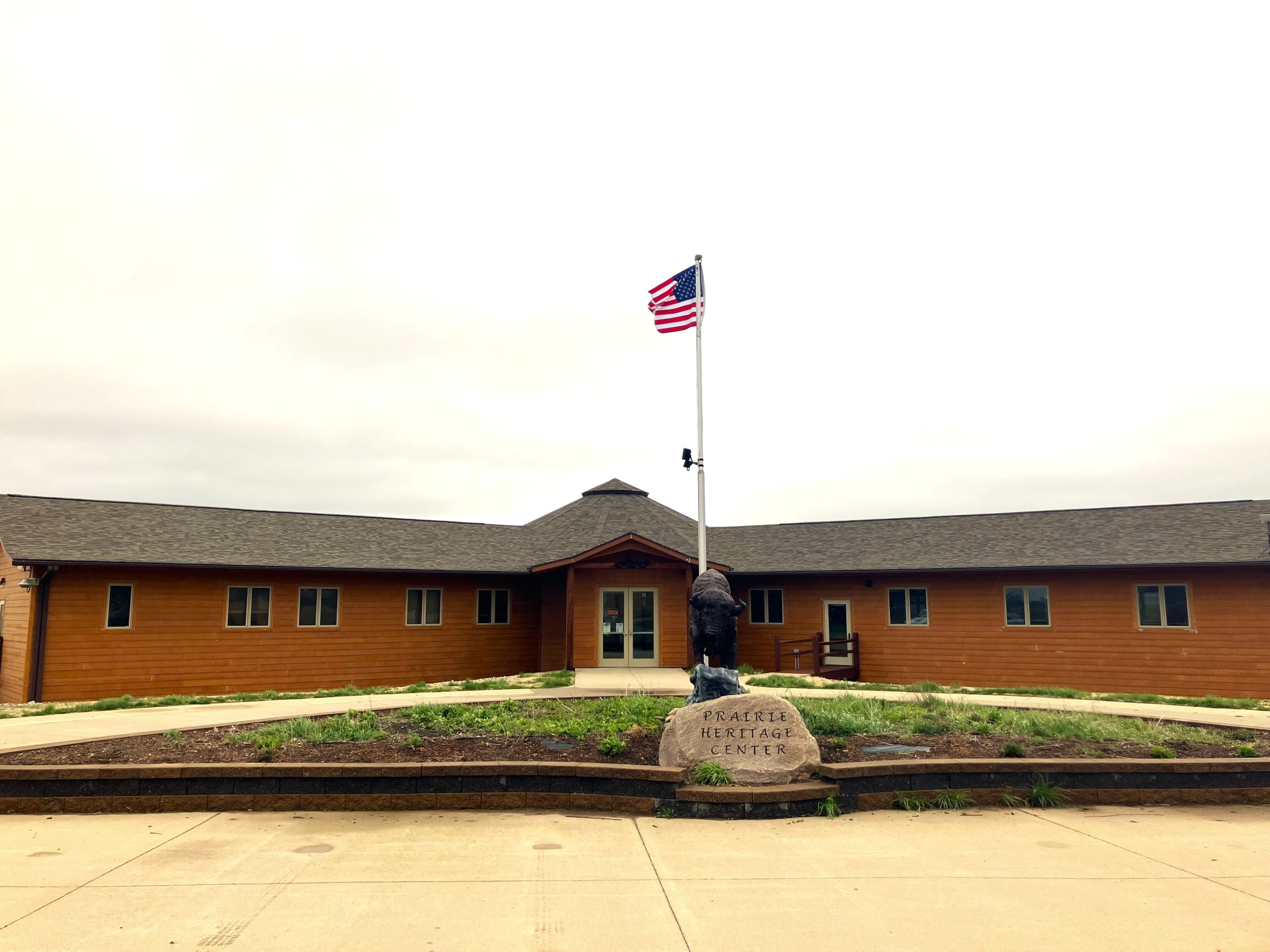 Wooden building with a gabled roof under a cloudy sky. An American flag flies on a pole.