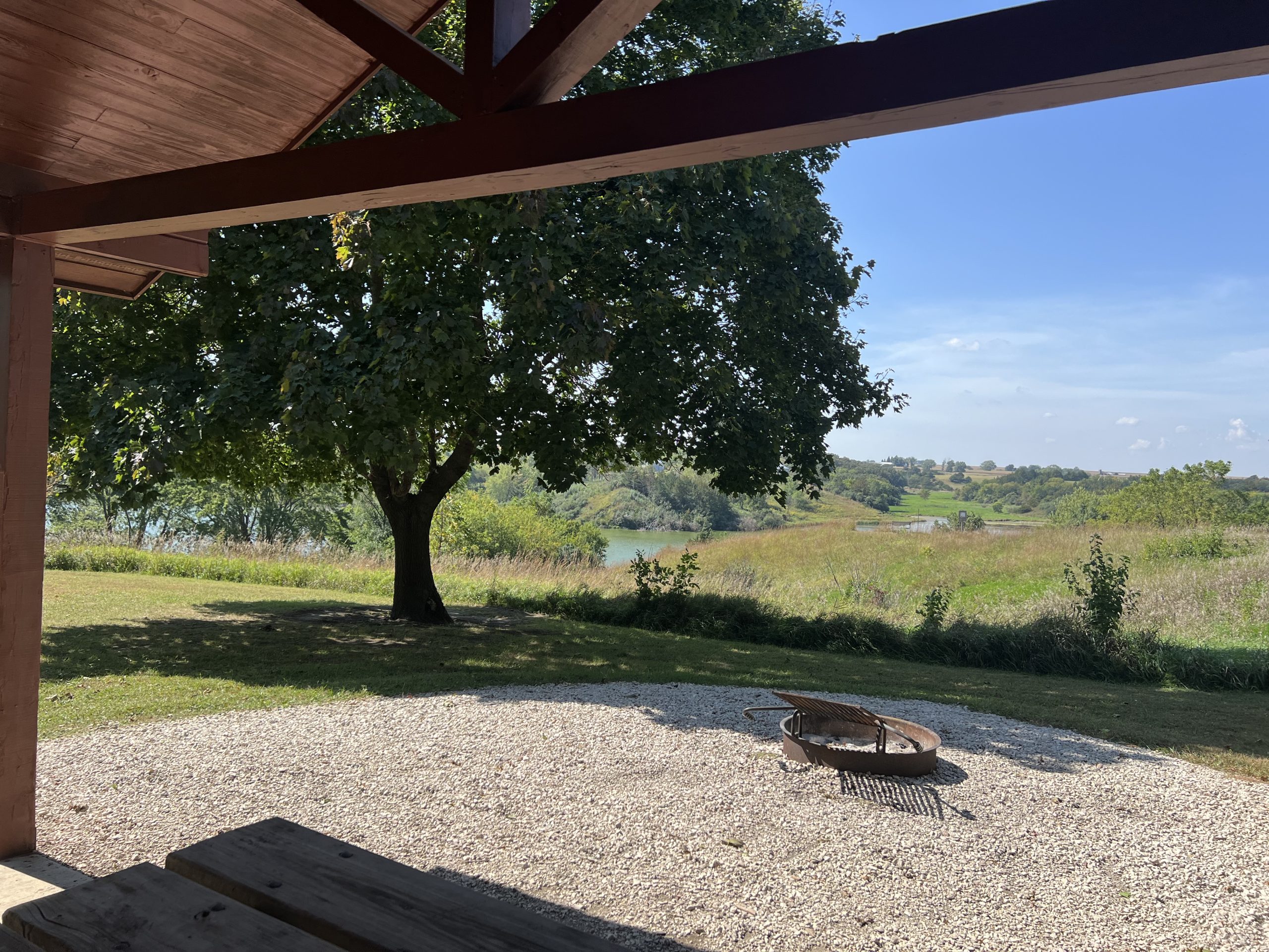 View of the lake from a cabin at Dog Creek Park with green grass, trees, blue sky.