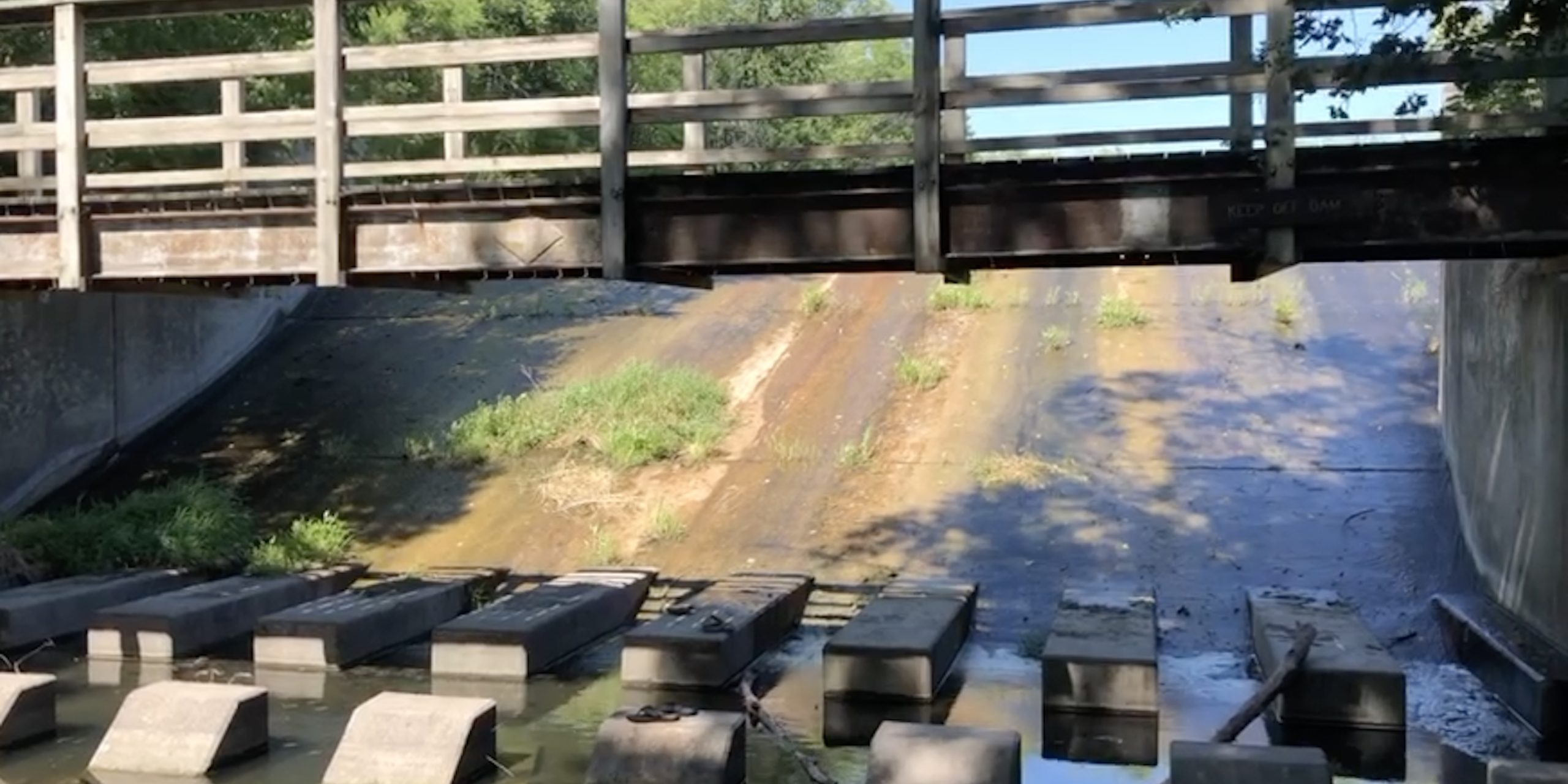 A wooden bridge spans over a concrete dam with water gently flowing beneath.