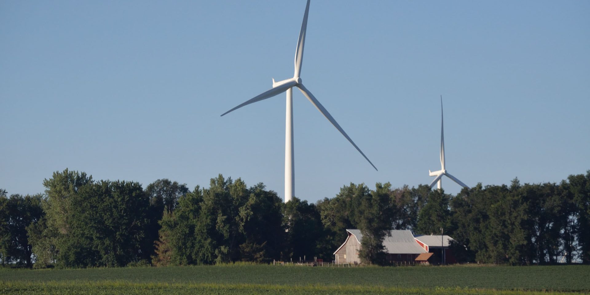 Windmill standing in the background with a farm and trees.
